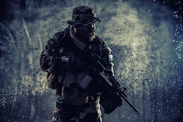 Commando fighter, professional mercenary, special forces soldier with camouflaged face, loaded with ammunition, armed assault rifle, patrolling on secret mission, sneaking in darkness ready to fight