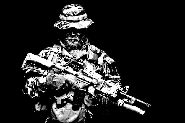 Commando shooter, army special forces rifleman in battle\
uniform, boonie hat, ammunition in load carrier, camouflaged with\
paint face, armed assault rifle, half length portrait on black\
background