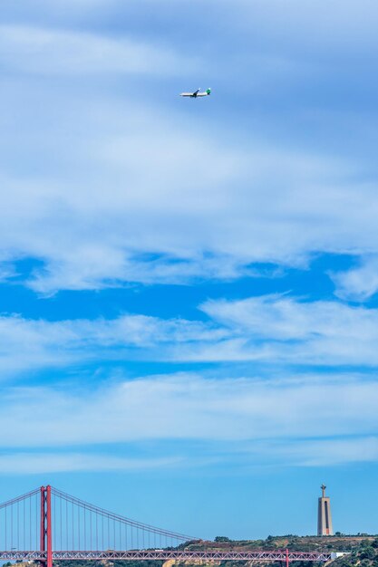 Commercial airplane with tourists flying over the red steel 25 de Abril suspension bridge