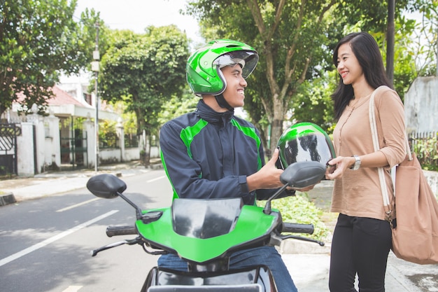 Commercial motorcycle taxi driver giving helmet to his customer