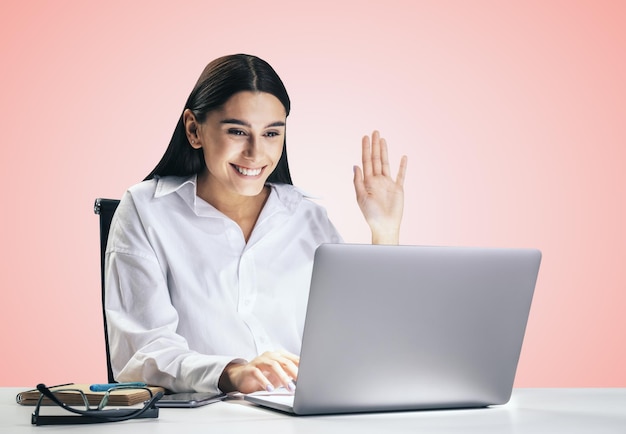 Photo communication concept with young pretty woman chating with collegue via online video service by laptop isolated on light pink wall background close up