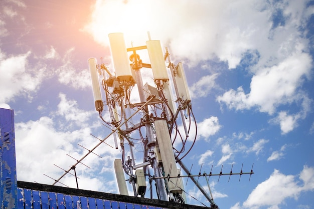 Communication tower with antennas on the top of building and bright blue sky with sun flare