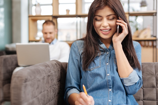 Comunicazione con le persone. bella donna positiva allegra che sorride e che parla con qualcuno al telefono mentre si gode il suo lavoro