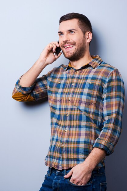 Фото Общение с удовольствием. красивый молодой человек в рубашке держит мобильный телефон и смотрит в сторону, стоя на сером фоне