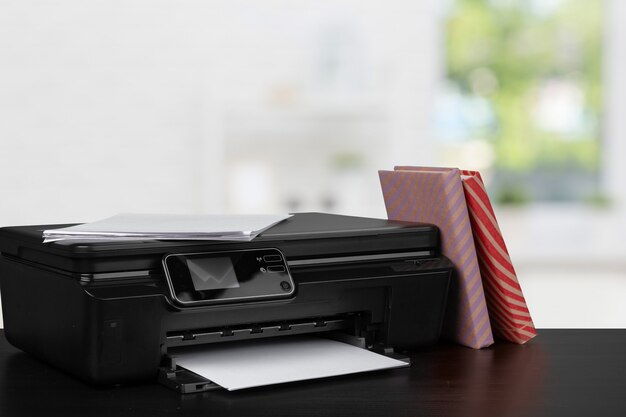 Compact home printer on desk with books against blurred background