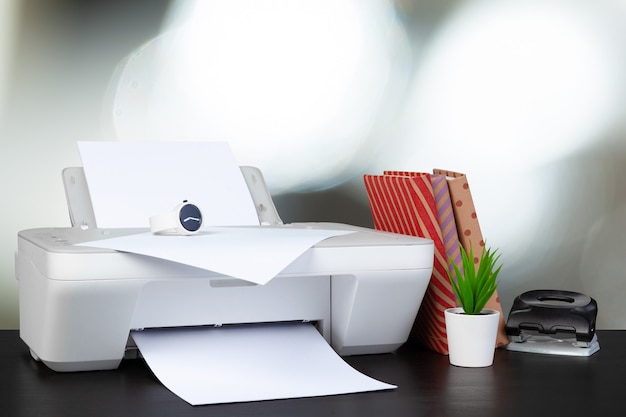 Compact home printer on desk with books against blurred background