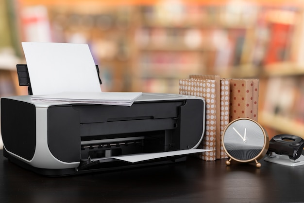 Compact home printer on desk with books against blurred background