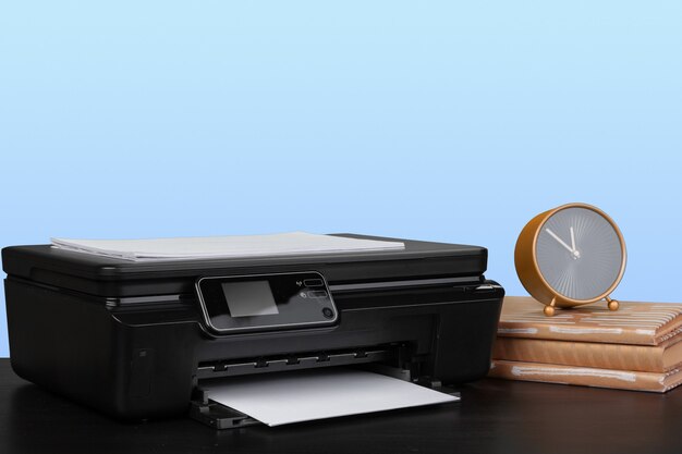 Compacte laserprinter op zwart bureau tegen blauwe achtergrond