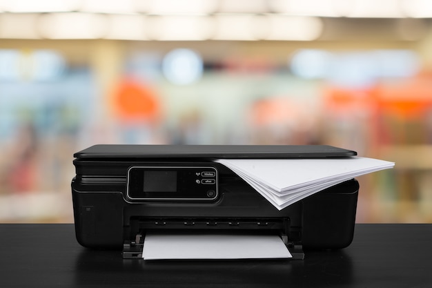 Compacte laserprinter op zwart bureau tegen onscherpe achtergrond