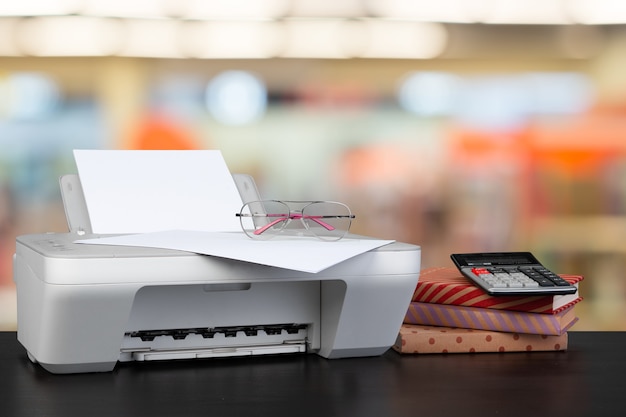 Compacte thuisprinter op bureau met boeken tegen onscherpe achtergrond