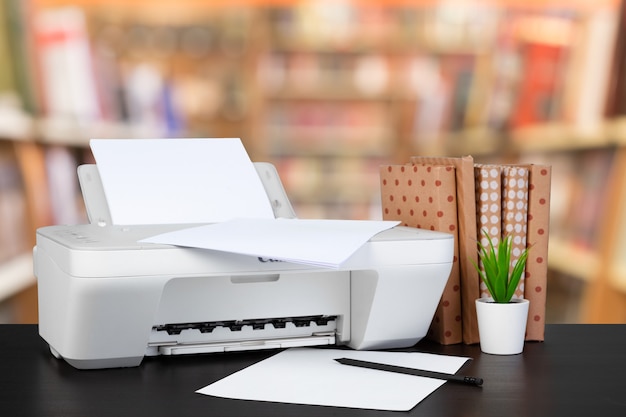 Compacte thuisprinter op bureau met boeken tegen onscherpe achtergrond