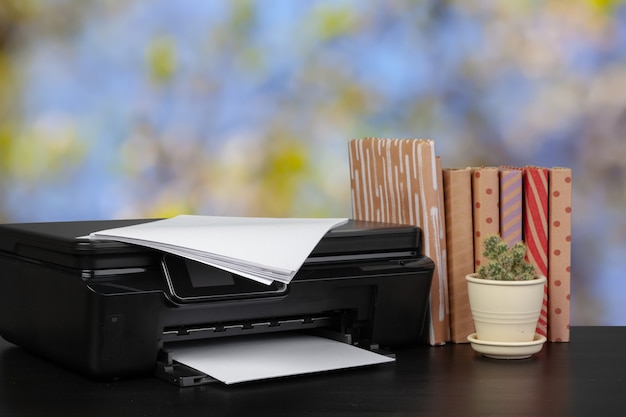 Compacte thuisprinter op bureau met boeken tegen onscherpe achtergrond