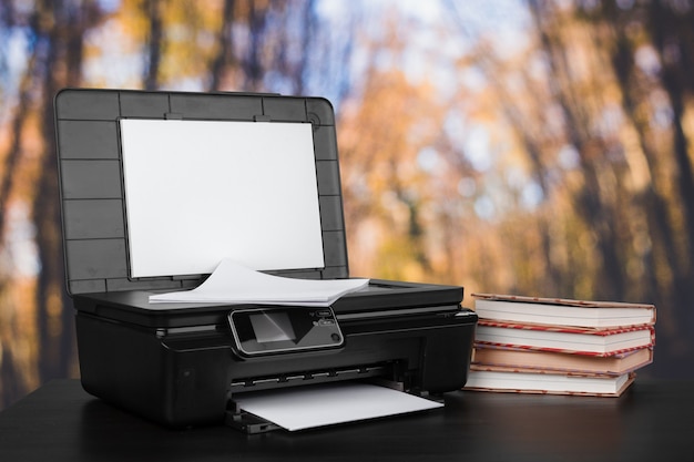 Foto compacte thuisprinter op bureau met boeken tegen onscherpe achtergrond