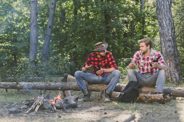 Company adult friends relaxing near campfire group of two male
backpackers relaxing near campfire two friends lumberjack worker
sitting in the forest and drinking beer