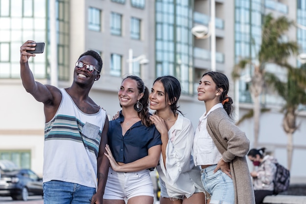 Company of cheerful diverse friends taking selfie in city