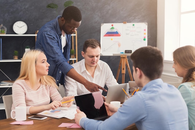 Company coworkers discussing ideas and brainstorming in office, black team leader controlling process, copy space