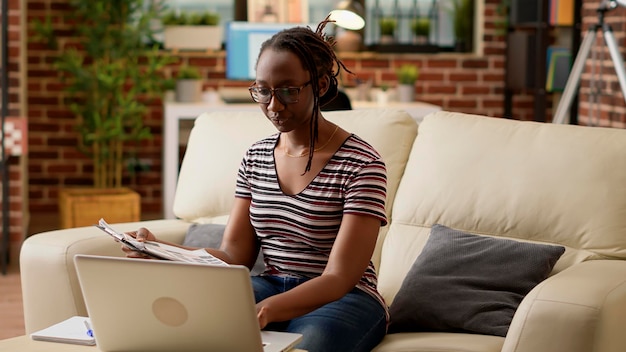 Company employee using laptop and paperwork to do remote job, browsing internet to work remotely on startup business. Young adult working from home on computer with online network.