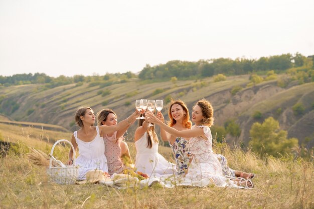 The company of female friends enjoys a summer picnic and raise glasses with wine