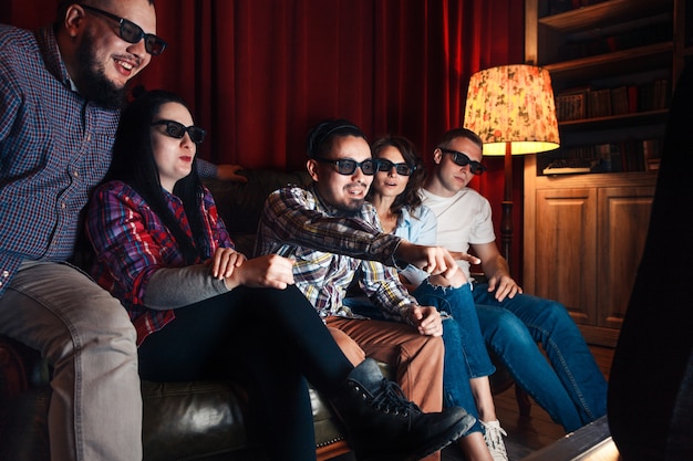 Company of five young friends excited watch movie in 3d glasses at home on couch