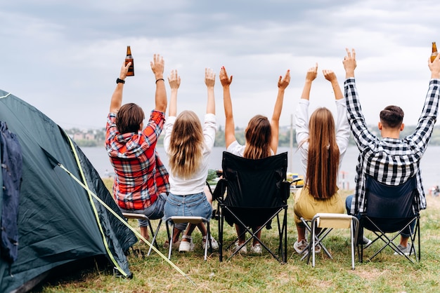 A company of friends have a lunch in the camping. They hands up. - Back view