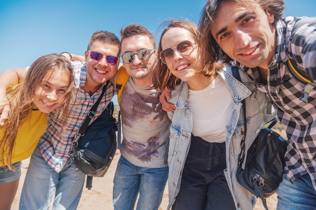 Foto gruppo di società di giovani graziosi abbraccianti felici, uomini e donne degli studenti su una spiaggia soleggiata, concetto di giorno di amicizia di viaggio di vacanza