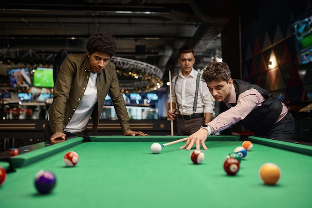 Company of handsome young guy playing in pool