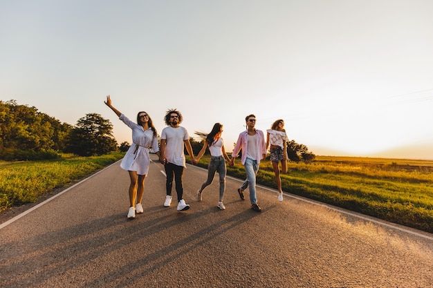 Company of happy young stylish guys walk on a country road on a sunny day .