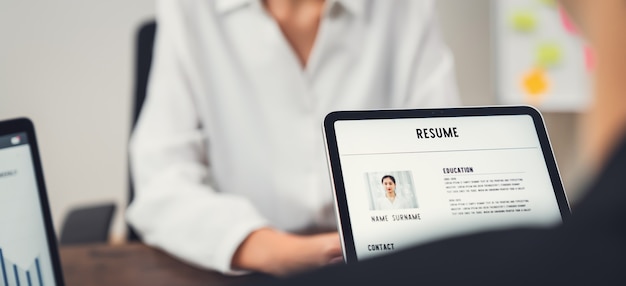 Company human resource (hr) houdt een cv-applicatie op tablet in de hand. jonge aziatische vrouw praten om sollicitatiegesprekken te geven.