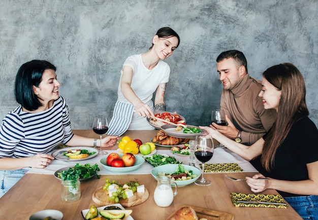 Company of men and women at home at a set table with drinks and food having fun and chatting