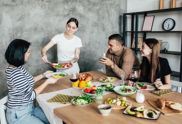 Company of men and women at home at a set table with drinks and food having fun and chatting