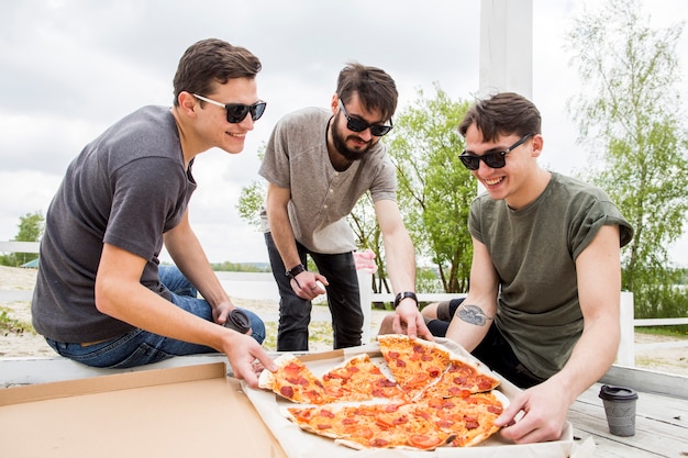 Company of smiling friends eating pizza on picnic