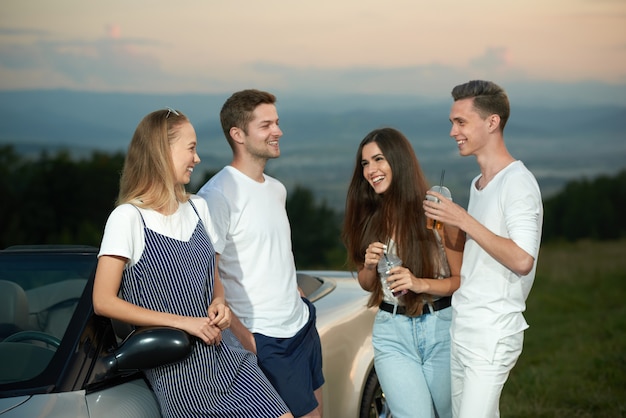 Company standing near cabriolet, smiling and communicating.