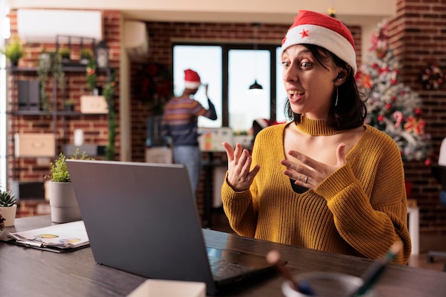 회사 직원은 크리스마스 트리와 축제 장식으로 사무실에서 화상 통화 회의에 대해 이야기합니다. 직장에서 휴가철 동안 원격 원격 화상 회의 및 온라인 회의에 참석합니다.