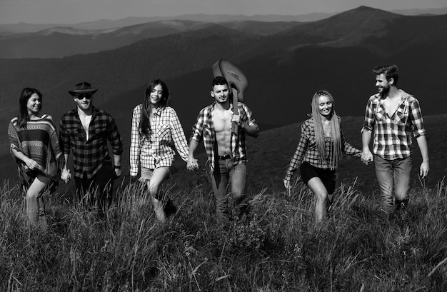 company of young active friends of boys and girls hiking in mountain countryside summer music