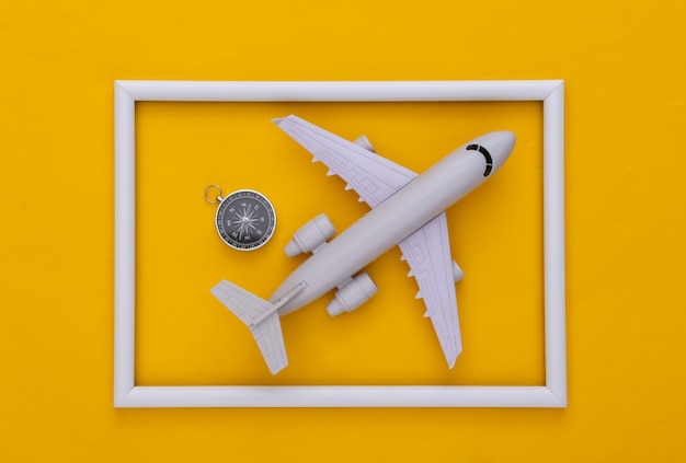 Compass and air plane in white frame on yellow background. Top view. Minimalism travel concept. Flat lay