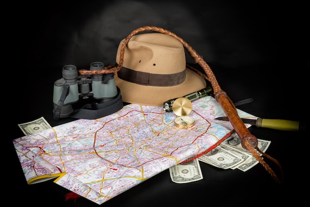 Foto bussola sulla mappa della città con torcia, cappello fedora, bullwhip, binocolo, coltello e banconote da un dollaro