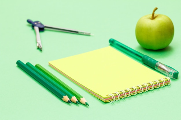 녹색 배경에 나침반, 색연필, 노트북, 펜, 사과. 학교 개념으로 돌아가기. 학용품. 필드의 얕은 깊이.