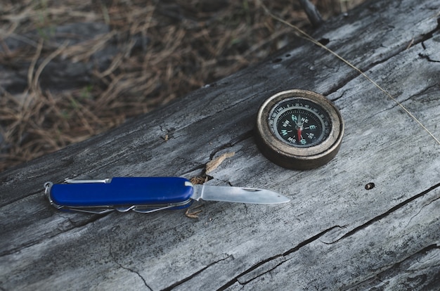 Compass and knife for survival in pine forest on log.