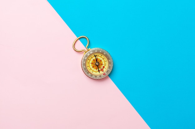 Compass on pink and blue background, top view