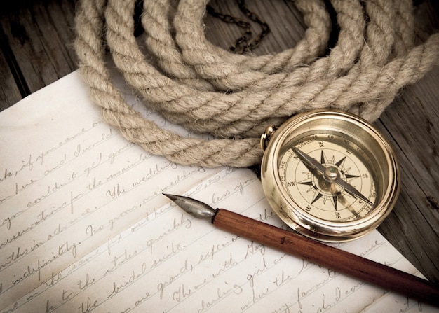 Compass, rope, pen and letter on an old paper on a wooden background close up