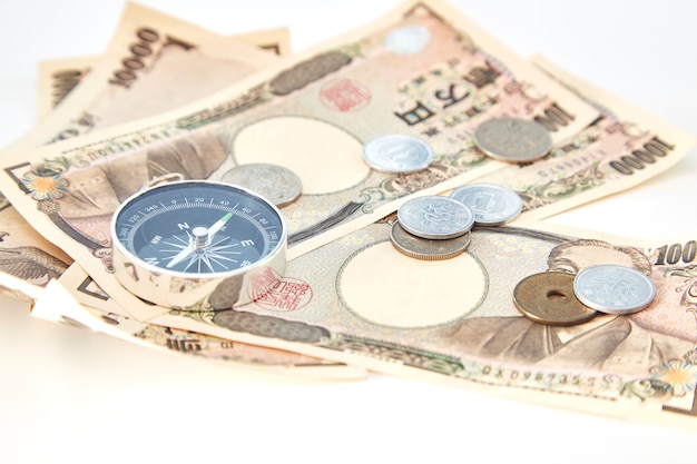 Фото Компас с банкнотами японской иены и монеты японской иены на белом фоне