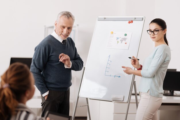 Competent female keeping highlighter in right hand raising eyebrows while standing near smart board