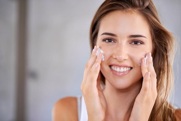 Photo complete skin care shot of a beautiful woman applying moisturizer to her face