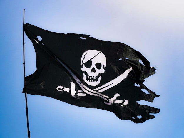 사진 완전히 찢어지고 멍이 든 검은 색 해적 깃발 (jolly roger)이 깃대에 고정되어 펄럭입니다.