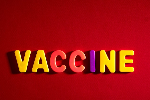 Photo completing vaccine words. vaccine word made from colourful plastic baby development blocks. red background