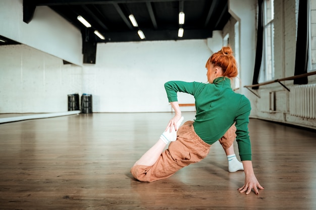 Complicated asana. Professional yoga coach wearing a green turtleneck doing complicated asana