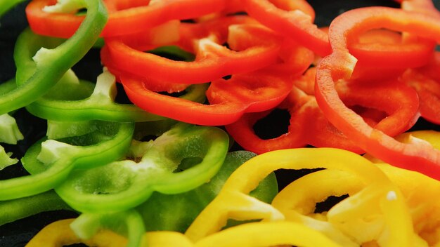 Photo composed heap of cut rings of green and yellow and red bell peppers in closeup