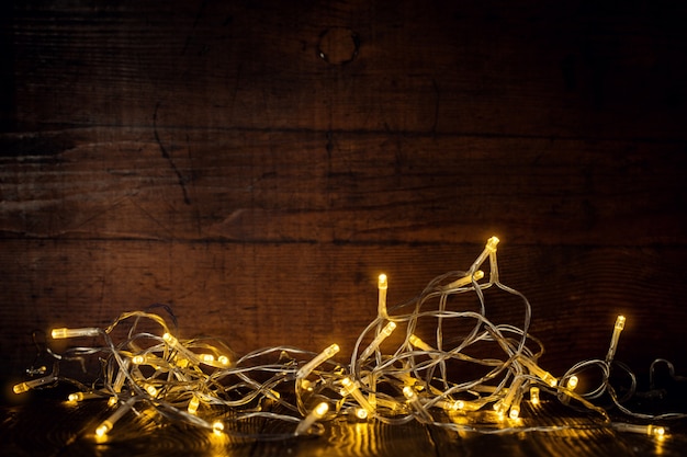 Photo composed lights of garland burning in dark on wooden background.