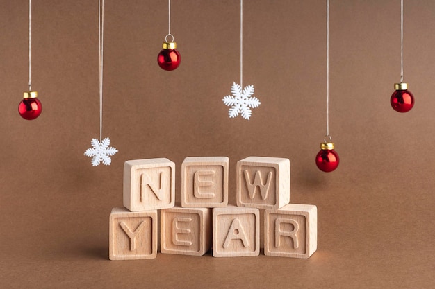 Foto composto la parola anno nuovo da cubi di legno su sfondo marrone fiocchi di neve e palle di natale cartolina di natale