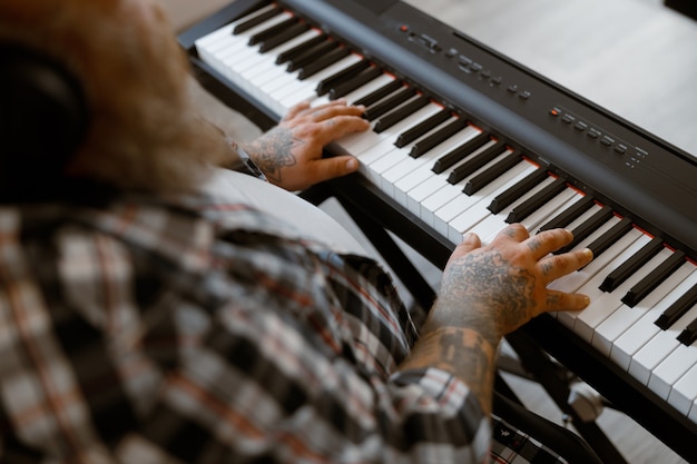 太りすぎの作曲家は、明るい部屋に座っている現代のシンセサイザーで音楽を再生します